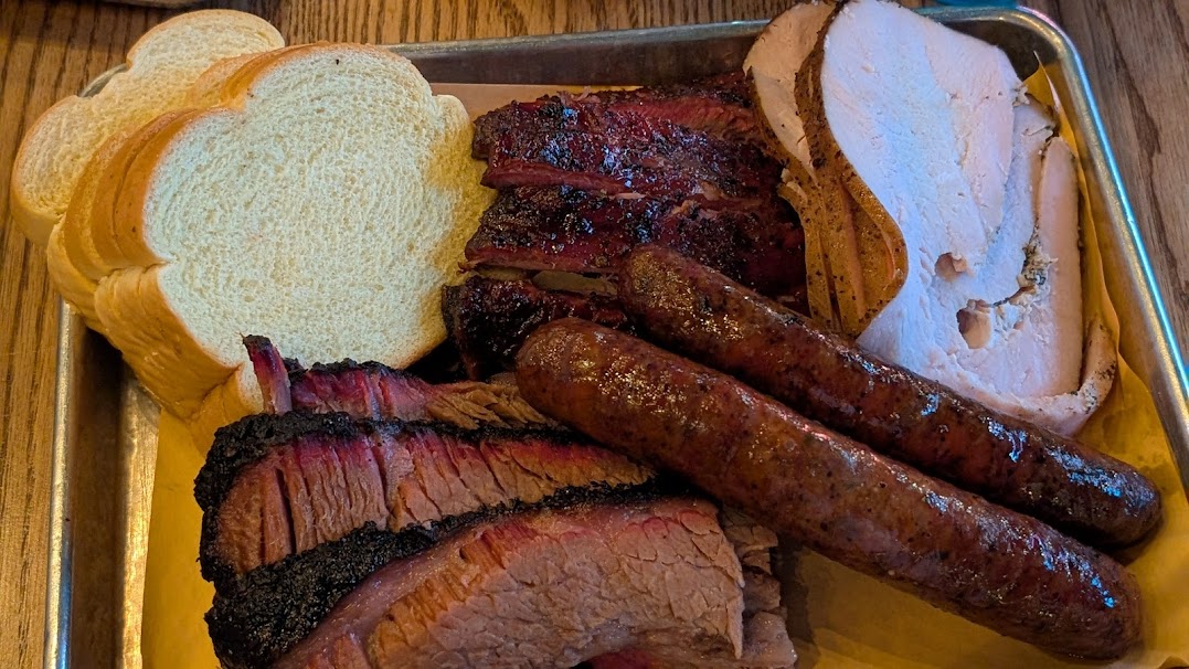 A platter of sliced brisket, sausage, and turkey with white bread.